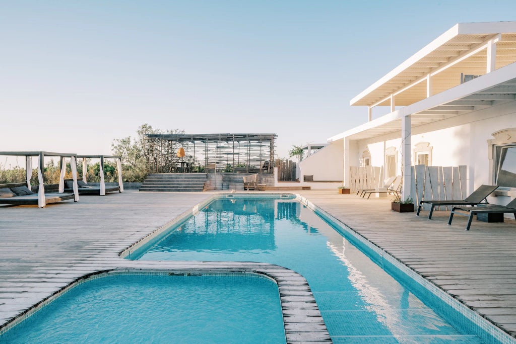 Luxury boutique hotel nestled in Portuguese countryside, with rustic wooden veranda, lush green landscape, and traditional architectural charm at sunset