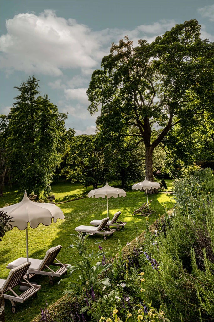 Contemporary luxury countryside hotel with stone facade, expansive green lawns, manicured gardens, and modern architectural elements nestled in lush Cotswolds landscape