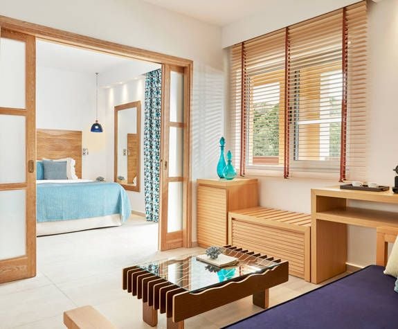 Elegant junior suite at Eagles Palace hotel with panoramic Aegean Sea view, featuring plush white bedding, modern decor, and private balcony overlooking turquoise waters