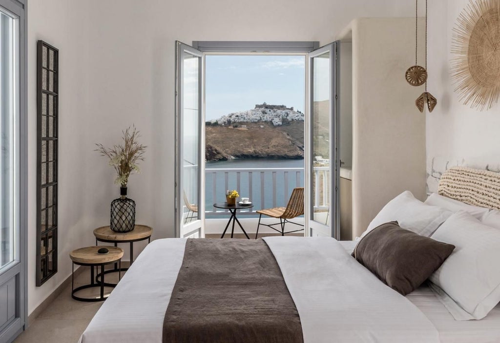 Elegant honeymoon suite in Greece with white-washed walls, luxurious bed, and breathtaking Aegean Sea view from private balcony at sunset