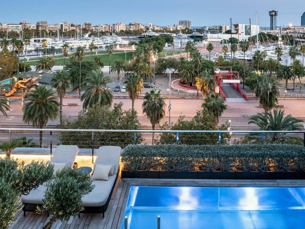 Luxury boutique hotel balcony overlooking Barcelona's Gothic Quarter, with elegant furnishings and stunning cityscape view at sunset