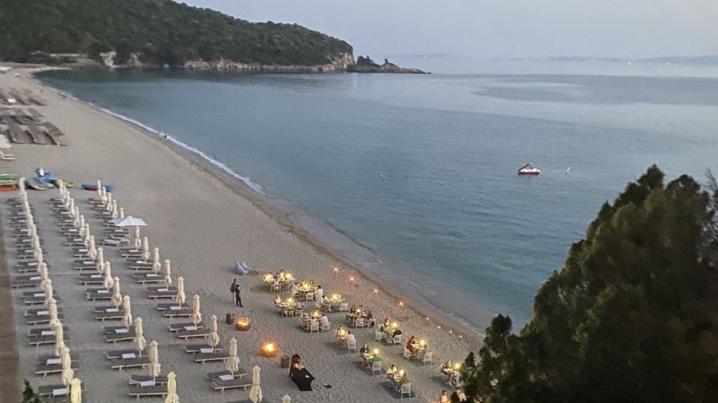 Luxurious beachfront hotel with sleek white architecture, infinity pool overlooking azure Ionian Sea, and minimalist Greek island design at sunset