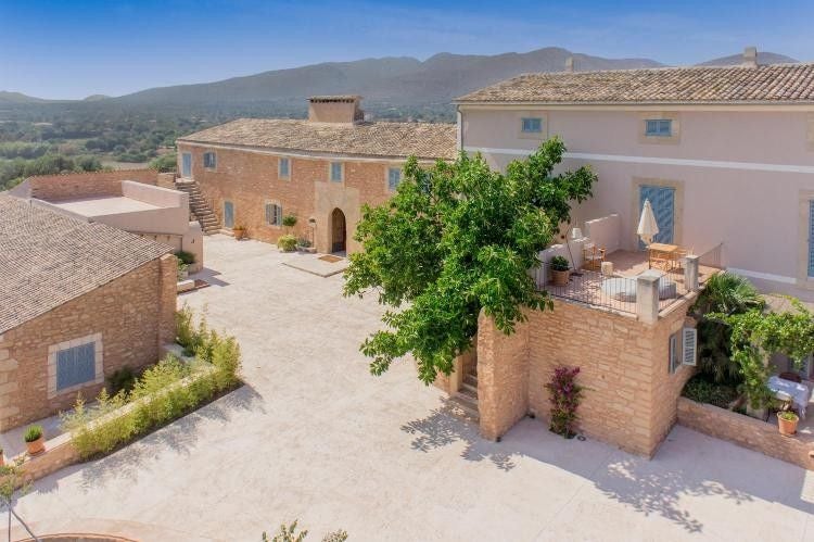 Luxurious Spanish countryside hotel with stone walls, terracotta roof tiles, and elegant outdoor lounge area surrounded by olive trees