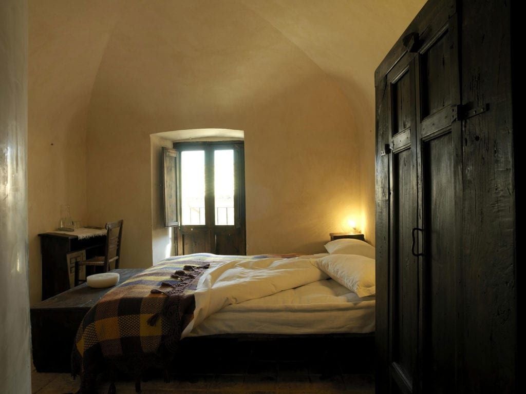 Rustic stone-walled hotel room in Santo Stefano di Sessanio, featuring antique wooden bed, traditional Italian alpine decor, warm natural lighting