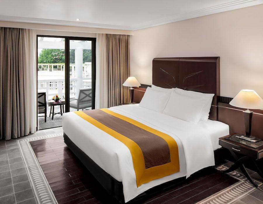 Elegant deluxe hotel room with French colonial styling, overlooking serene Perfume River in Hue with warm wood furnishings and soft natural lighting