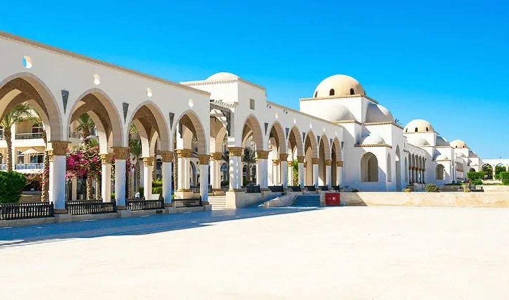 Elegant beachfront resort with white Arabian-style domes and arches overlooking pristine Red Sea waters and manicured palm gardens