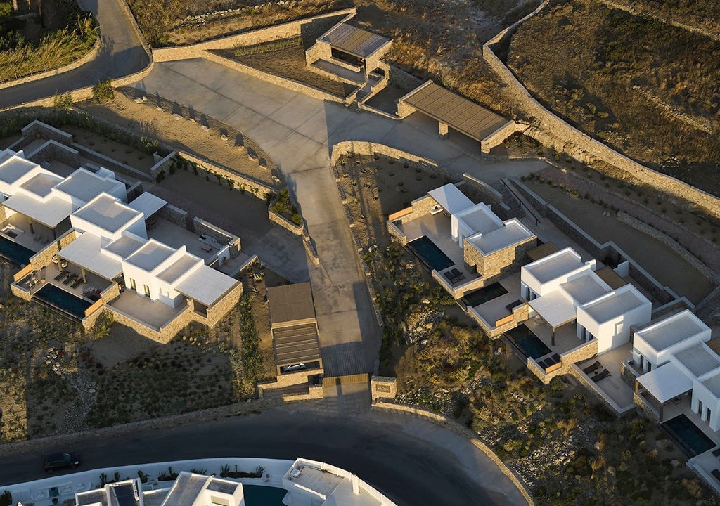 Luxury white-washed hotel overlooking azure Aegean Sea, traditional Cycladic architecture with blue-domed roofs and sun-drenched terraces in Mykonos, Greece