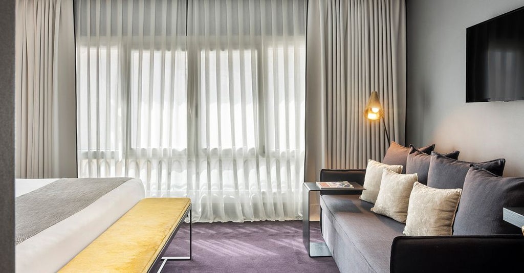 Elegant Madrid hotel room with expansive city skyline views, featuring plush king bed, modern decor, and large floor-to-ceiling windows bathed in warm sunlight