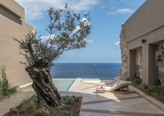 Modern Mediterranean suite with private infinity pool overlooking blue ocean, featuring white architecture and sunbeds at sunset