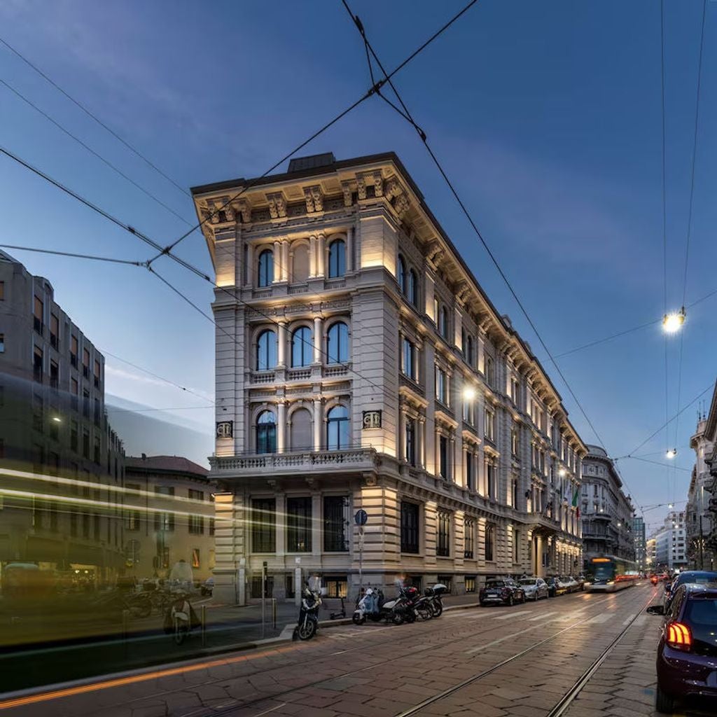 Art Deco-style historic hotel facade with ornate stone columns, grand arched windows, and elegant balconies in central Milan's cityscape