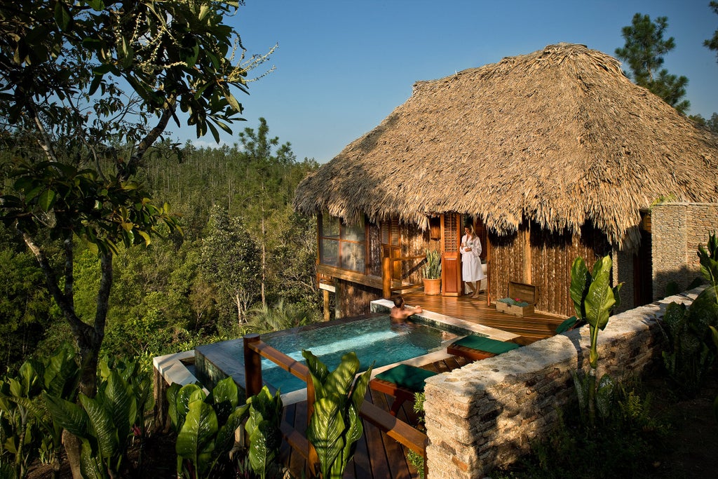 Elevated eco-luxury lodge nestled in Belize rainforest, featuring stone walls, thatched roof, and tropical gardens with mountain views