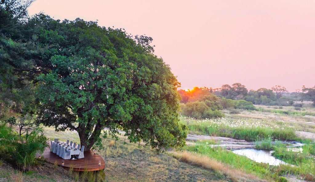 Luxurious open-air safari lodge with stone walls and thatched roof overlooking African wilderness, private pool reflecting sunset sky