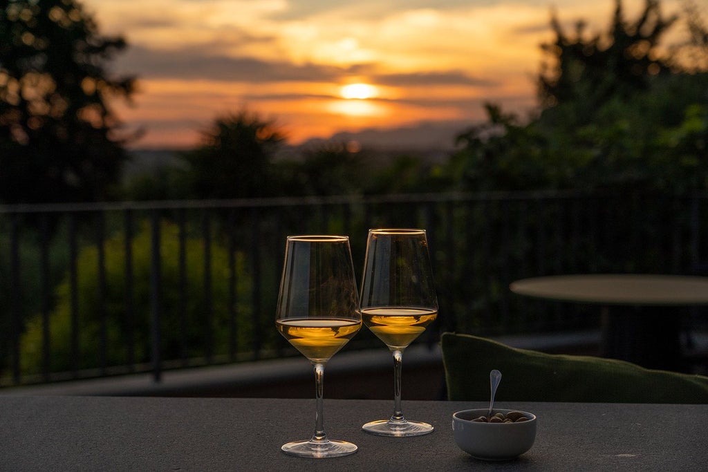 Rustic Tuscan luxury hotel nestled among rolling green hills, featuring elegant stone exterior, terracotta roof, and inviting outdoor seating area with panoramic countryside views