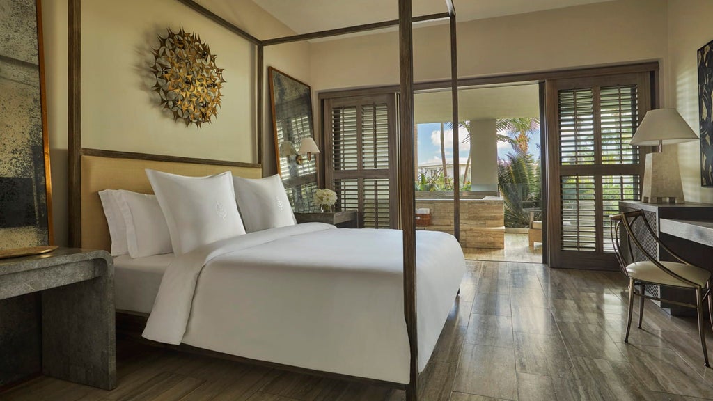 Luxurious hotel suite with floor-to-ceiling windows framing Caribbean views, modern furnishings, and a private balcony with infinity railing