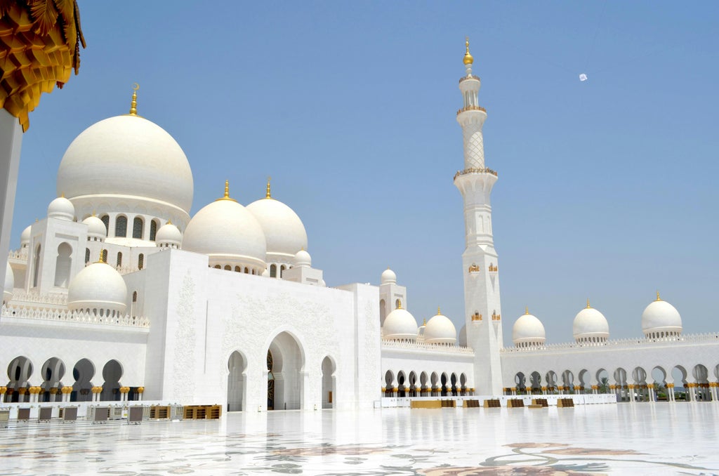 Grand Sheikh Zayed Mosque with gleaming white domes and ornate archways reflecting in pools under clear blue Abu Dhabi skies