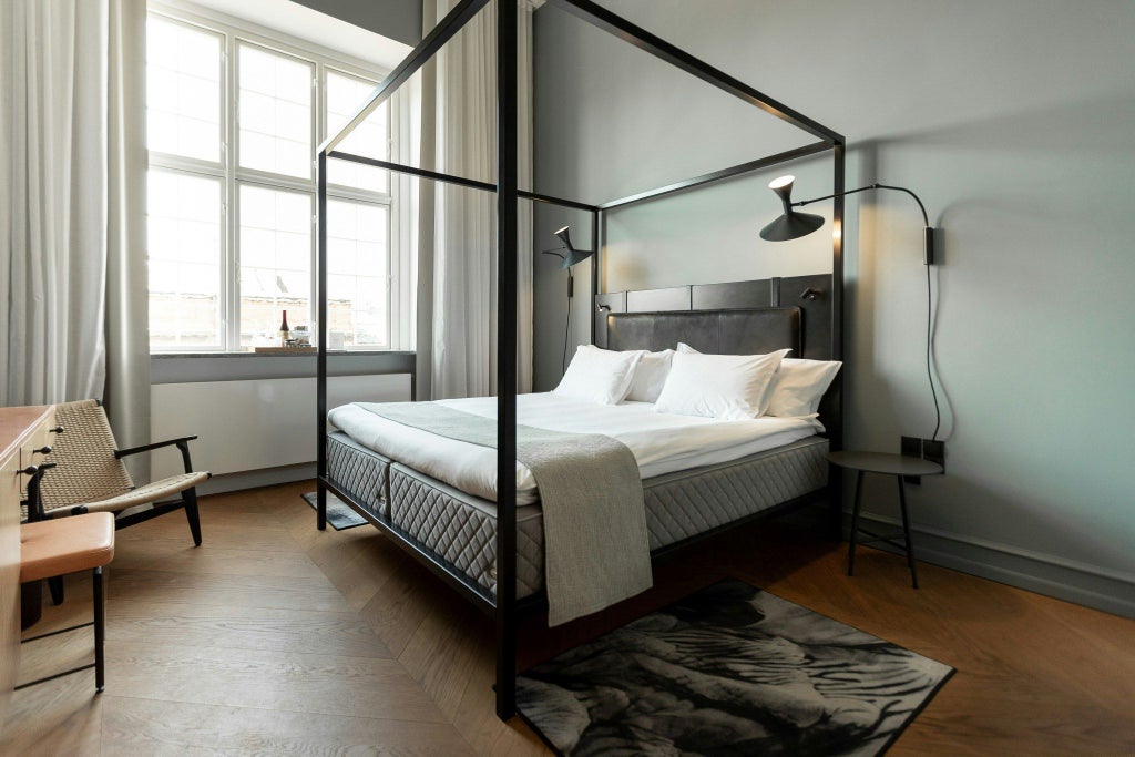 Elegant Scandinavian hotel room with minimalist design, warm wood tones, plush white bedding, and contemporary furnishings at a luxury Copenhagen hotel