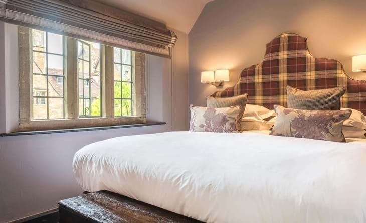 Elegant classic room with plush king bed, antique wooden furnishings, soft cream walls, and charming period details at historic Lygon Arms hotel in British countryside