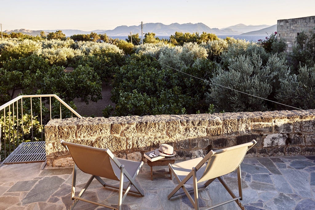 Sunlit stone villa with terracotta roof overlooking azure Aegean Sea, surrounded by olive groves and traditional Greek landscape at golden hour