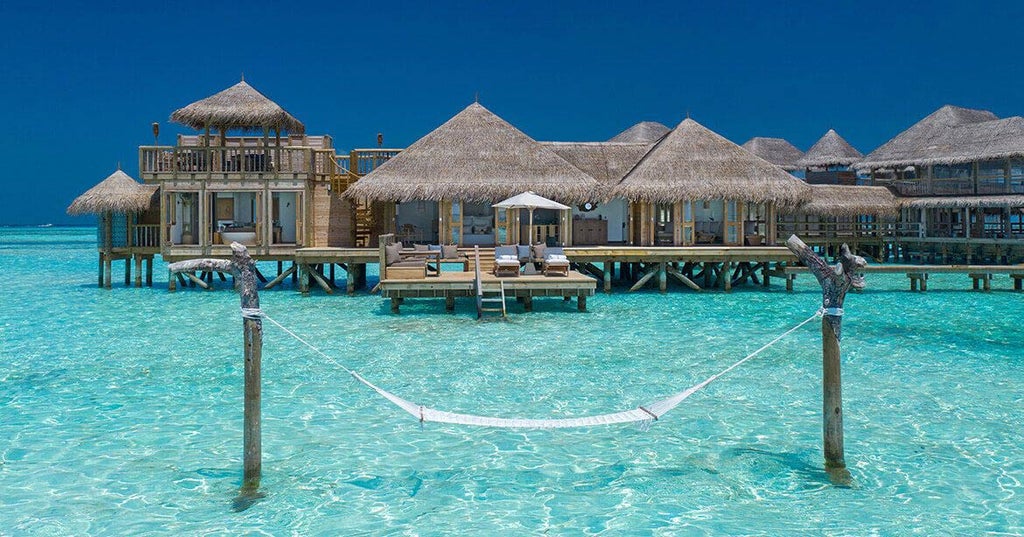 Luxurious overwater villa at Gili Lankanfushi resort with wooden boardwalk, turquoise lagoon waters and palm trees at sunset