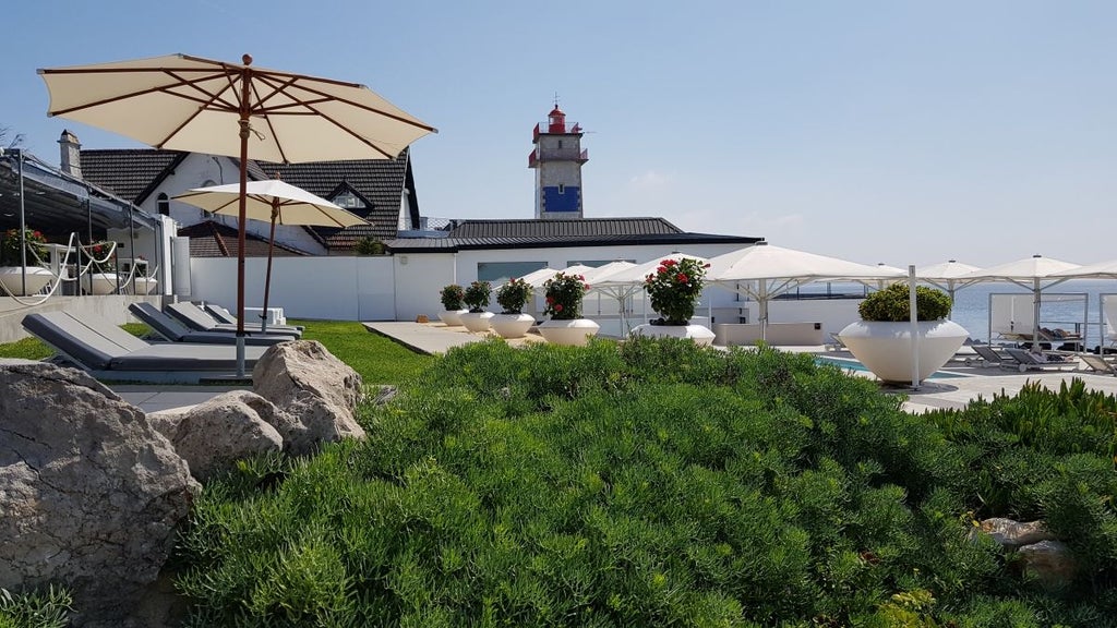 Luxurious whitewashed coastal hotel with blue-trimmed balconies overlooking azure waters of Portuguese shoreline near scenic cliffs and rocky landscape