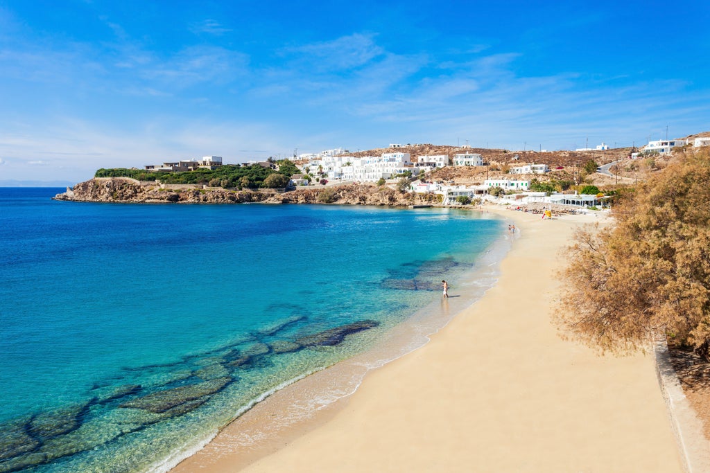 Pristine white buildings with blue domed roofs cascading down Mykonos hillside, overlooking the sparkling Aegean Sea at sunset