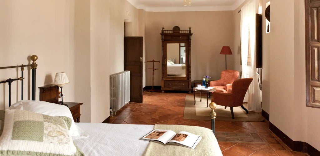 Elegant Spanish colonial-style bedroom with antique wooden furnishings, white linens, and ornate architectural details at Cortijo del Marqués estate