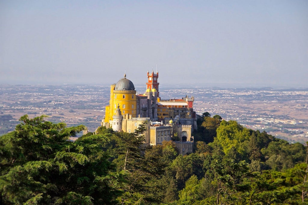 Colorful historic Pena Palace on hilltop, vibrant tiled facades, lush green landscapes of Sintra with glimpse of elegant coastal town Cascais in distance