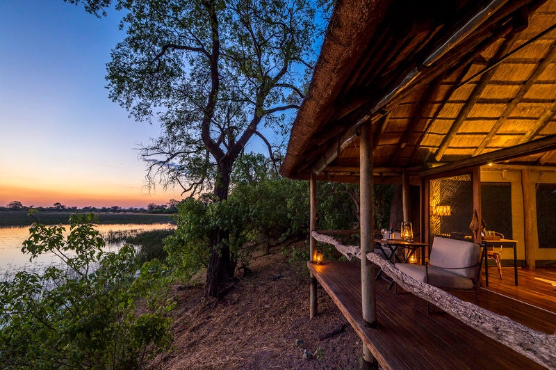 Elevated safari lodge with private wooden deck overlooking African savanna, featuring plush seating and canvas tent accommodations