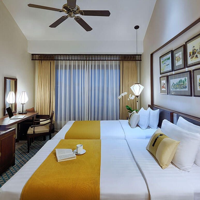 Elegant Vietnamese boutique hotel room with soft cream walls, wood accents, plush white bedding, and traditional local design elements in warm tones