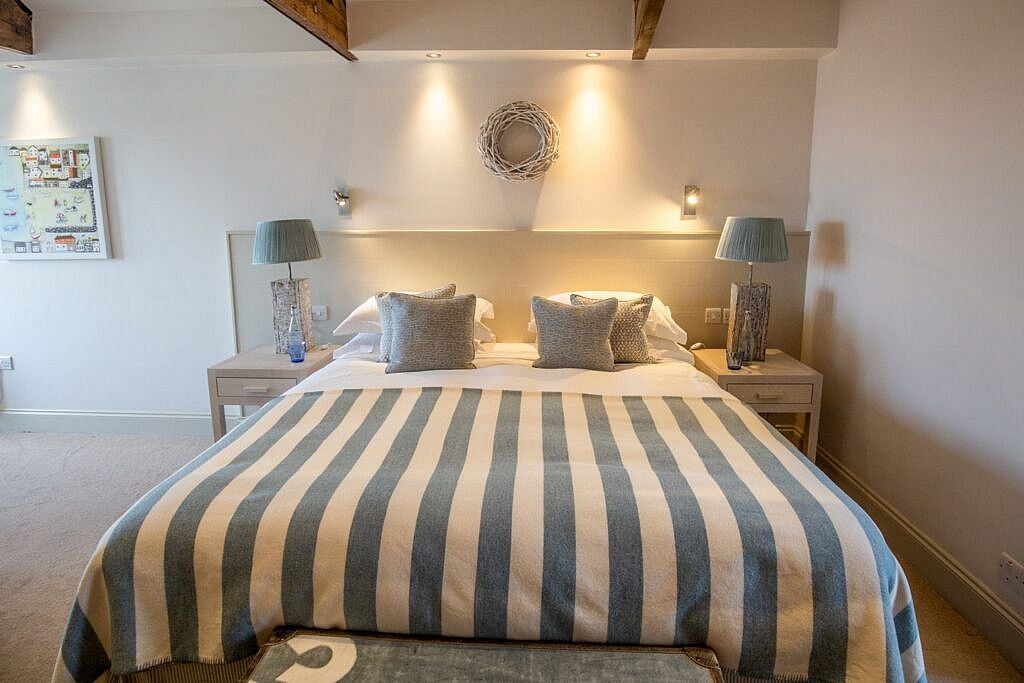 Elegant coastal hotel room with white linens, nautical blue accents, large window overlooking seaside, modern minimalist design in St Mawes, Cornwall