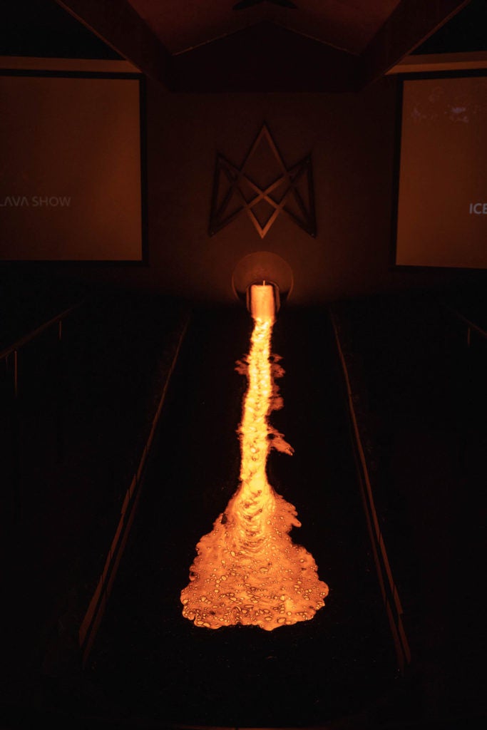 Indoor demonstration where bright orange molten lava flows dramatically on ice blocks, creating steam and showcasing its natural power