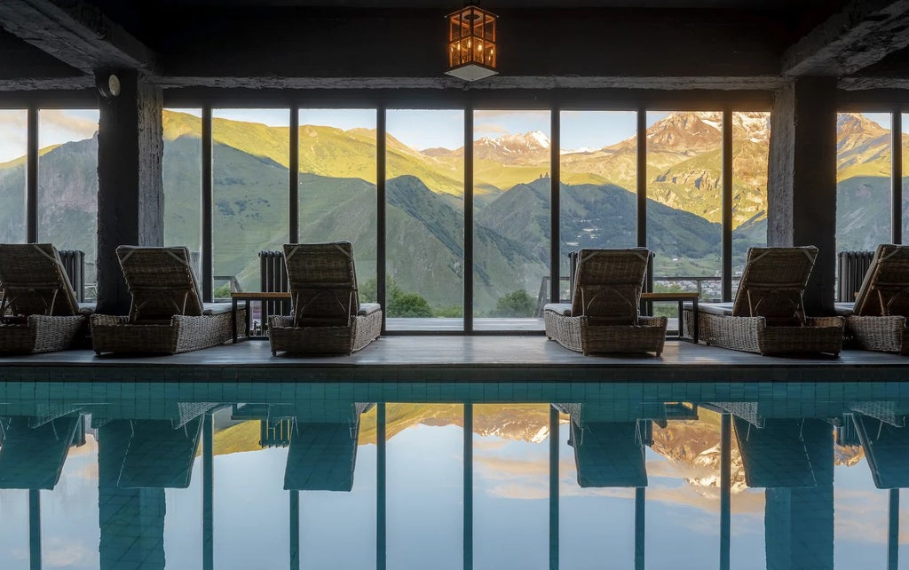 Luxurious mountain hotel with modern architecture, featuring expansive glass windows overlooking dramatic Kazbegi landscape and snow-capped peaks