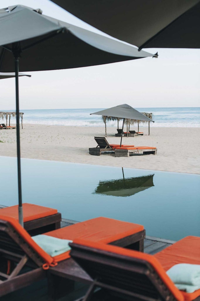 Luxurious beachfront hotel with minimalist white architecture, nestled against rugged Mexican coastline with palm trees and infinity pool at sunset