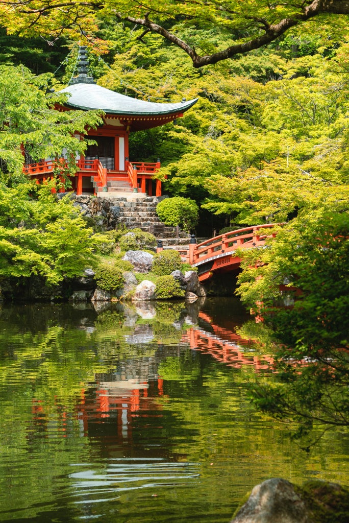 Traditional ornate red torii gate at Fushimi Inari Shrine in Kyoto, framed by lush green bamboo forest and stone lanterns at dusk