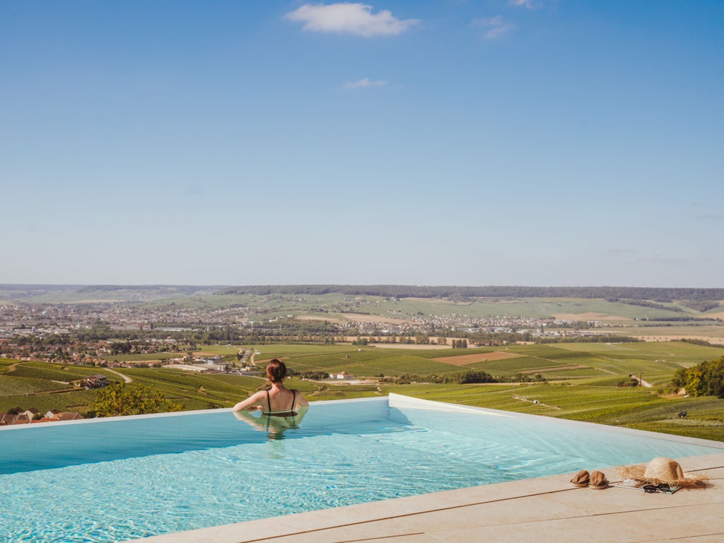 Elegant infinity pool overlooking French vineyards at sunset, with modern loungers and panoramic countryside views of Champagne region