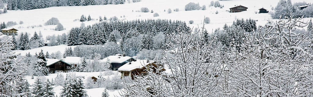 Luxurious wooden chalet bedroom in French Alps, featuring plush white bedding, rustic timber walls, and panoramic mountain landscape through large windows