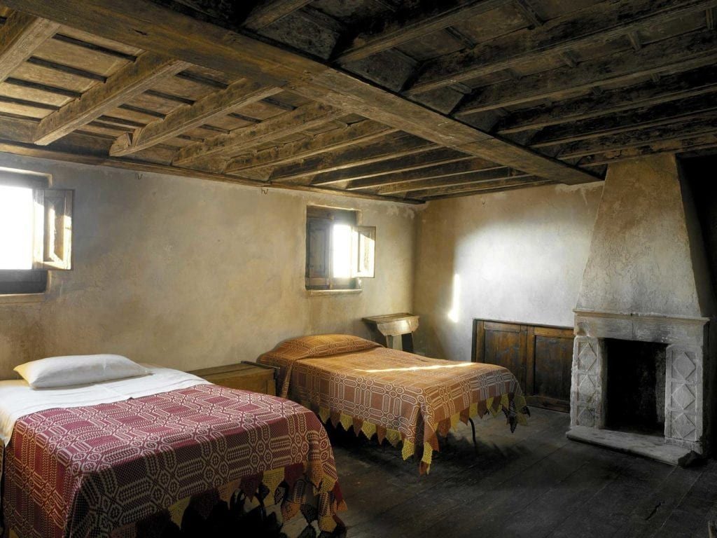 Rustic stone-walled superior room with warm wooden furnishings, traditional Italian elegance, soft natural light, and minimalist luxury in Sextantio Albergo Diffuso