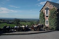 Rustic stone country hotel with warm glowing windows, nestled in lush green countryside of United Kingdom, featuring traditional architectural charm and inviting exterior.