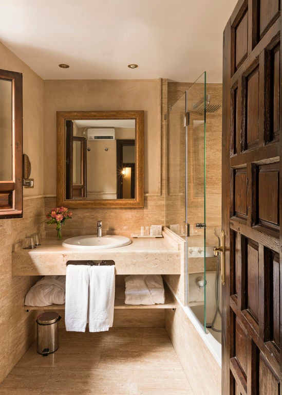 Elegant hotel room with ornate gold-framed mirror, crystal chandelier, antique wooden furniture, and plush white bedding in Granada