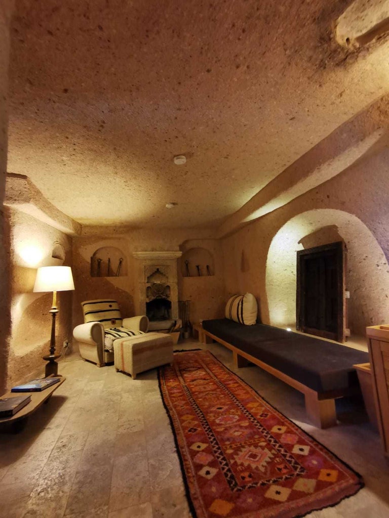 Elegant stone-walled junior suite with plush white bedding, arched windows overlooking Cappadocia's unique landscape, blending rustic charm and modern luxury