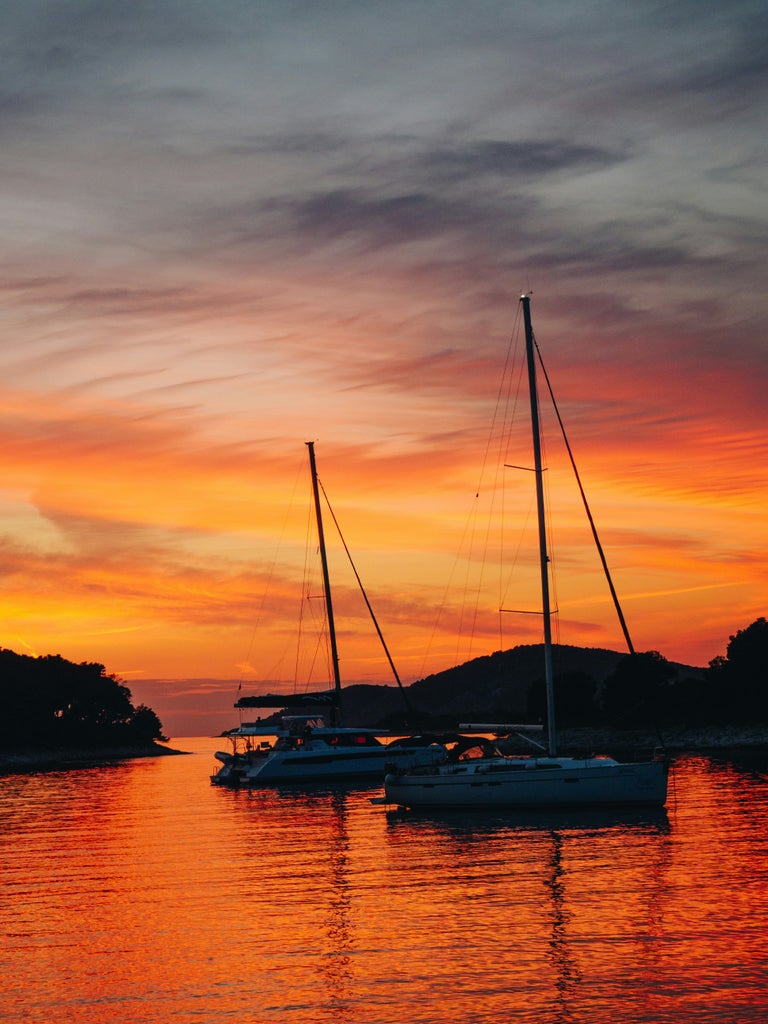 Sleek white yacht anchored in crystal-clear turquoise waters near Pakleni Islands, with Hvar's scenic coastline in the background