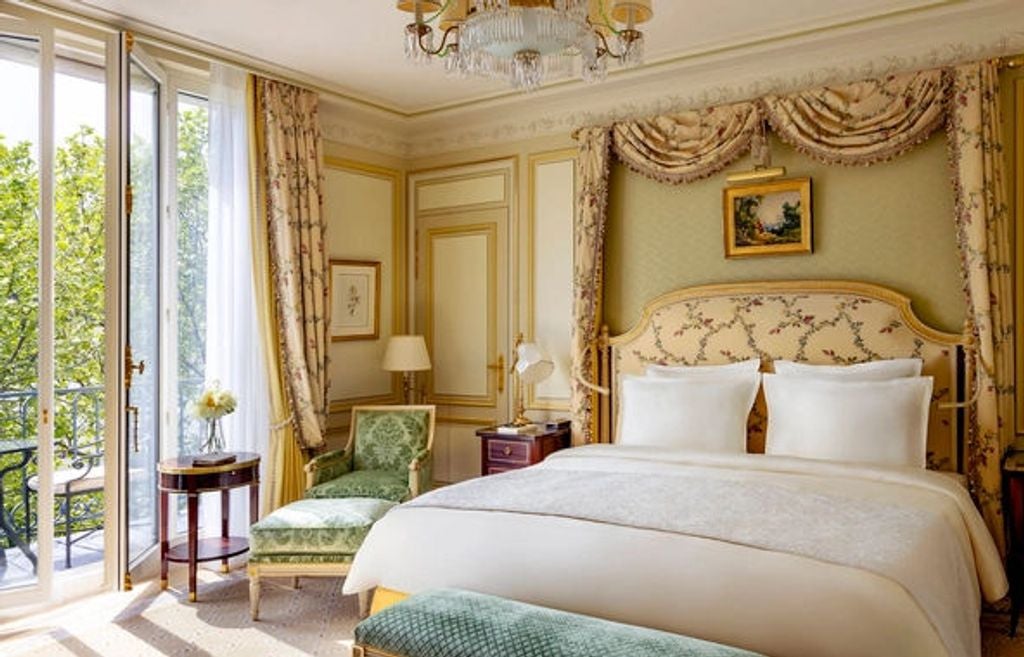 Elegant Ritz Paris deluxe room with gold-accented furniture, crystal chandelier, antique mirrors, and plush king bed with silk drapes