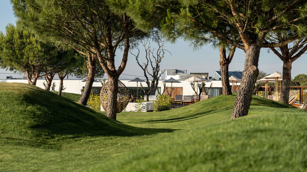 Modern luxury hotel exterior with curved white architecture, infinity pool surrounded by loungers and vast Alentejo countryside views