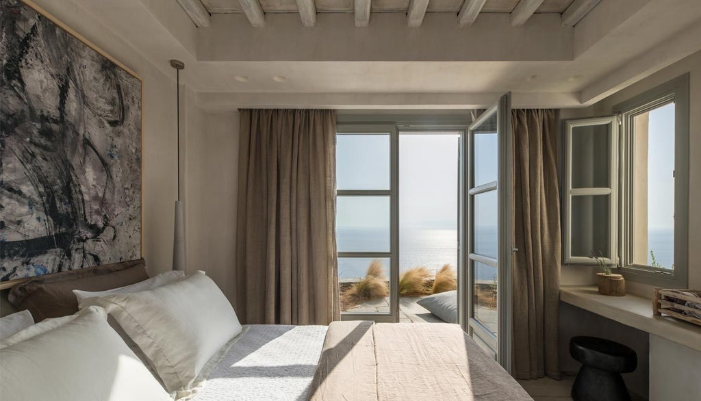 Minimalist white bedroom with blue Aegean Sea view, sleek wooden furniture, and private balcony at luxury boutique hotel in Sifnos, Greece.