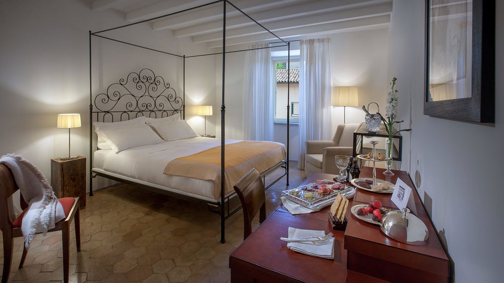 Elegant stone-walled suite with plush king bed, antique wooden furnishings, soft neutral tones, and expansive windows overlooking Umbrian countryside landscape