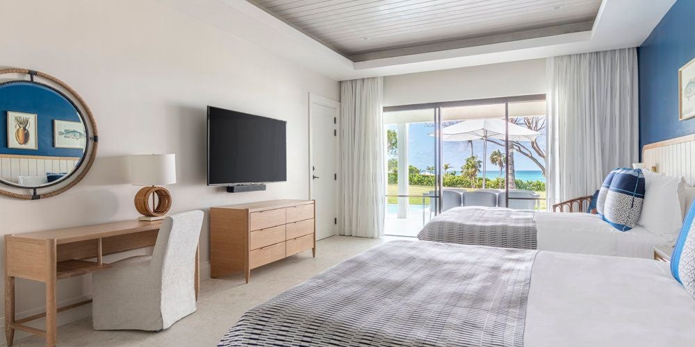 Luxurious family suite with ocean-facing balcony, featuring modern Caribbean decor, plush king bed, and elegant sitting area overlooking Antigua's turquoise waters