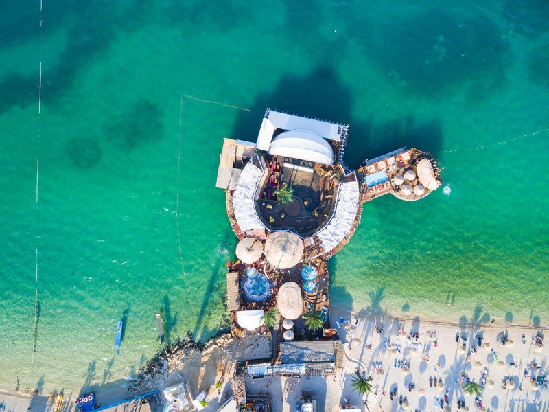 Sun-drenched harbor with luxury yachts moored along stone promenade of coastal Croatian town, backed by historic terracotta rooftops