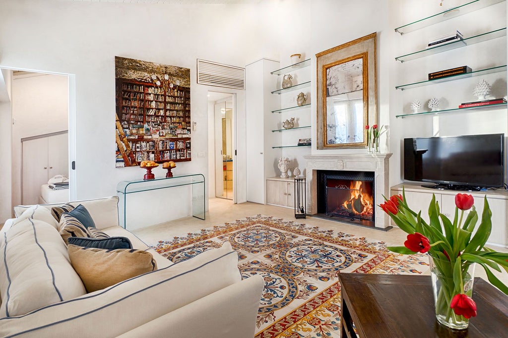 Elegant Sicilian hotel room with soft cream linens, antique wooden furnishings, arched window overlooking lush Mediterranean garden at Donna Coraly Resort