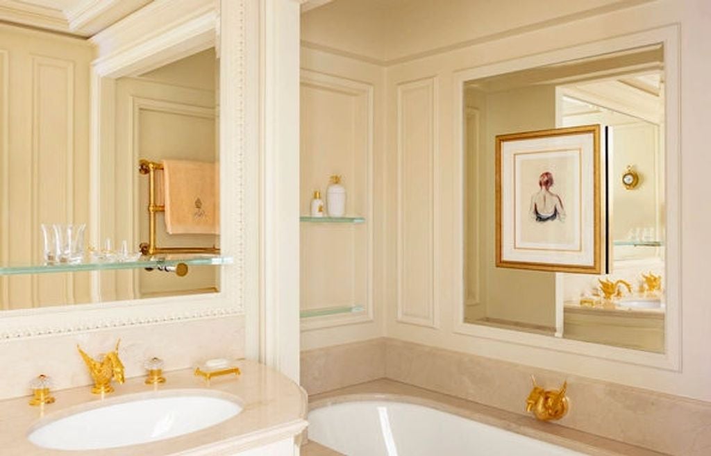 Opulent Parisian hotel room with crystal chandelier, gold-framed mirrors, ornate Louis XV furniture and silk-draped windows overlooking courtyard