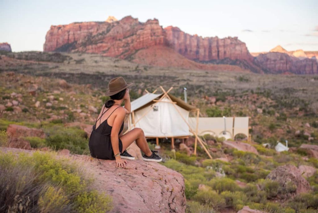 Luxurious safari-style canvas tent at sunset near red rock formations, overlooking scenic landscape of a national park wilderness area